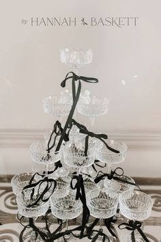 a tall glass cake stand with lots of glasses on it's top and black ribbon around the base