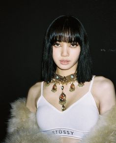 a woman with black hair wearing a white tank top and fur stole around her neck