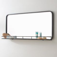 a bathroom mirror sitting above a shelf filled with personal care items on top of a white wall