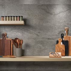 kitchen utensils and cutting boards sit on a shelf in front of a gray wall