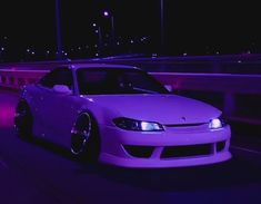 a white car parked on the side of a road in front of a bridge at night