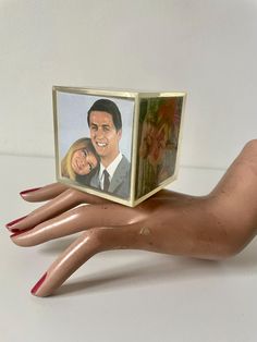 a hand holding a small photo cube with a woman's face on it and a man's head in the middle