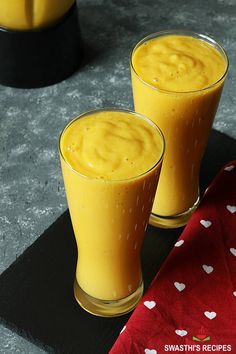 two glasses filled with yellow liquid sitting on top of a black tray next to each other