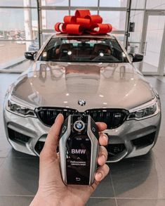 a person holding a cell phone in front of a bmw car with a bow on top