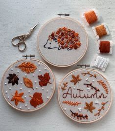 three embroidery hoops with autumn designs on them and some thread spools to the side