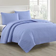 a blue quilted bedspread and pillows in a room with white furniture on the floor