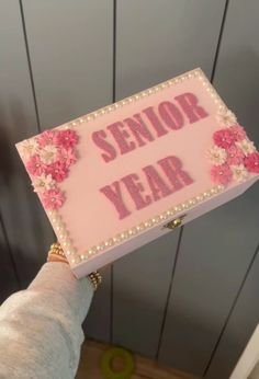 a person holding up a sign that says senior year with pink flowers and pearls on it