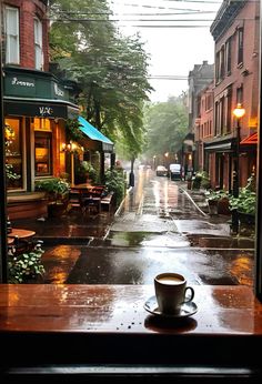 a cup of coffee sitting on top of a wooden table next to a window covered in rain