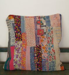 a multicolored patchwork pillow sitting on top of a wooden bench next to a white wall