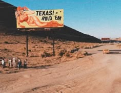 a billboard on the side of a dirt road with people standing in front of it