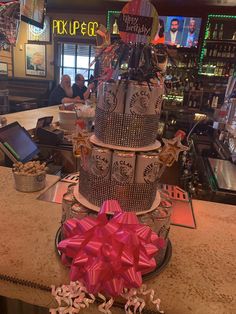 three tiered cake sitting on top of a counter with a pink bow tied around it