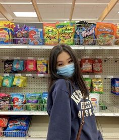 a woman wearing a face mask while standing in front of a store shelf filled with snacks