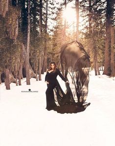 a woman is standing in the snow with an animal statue behind her and sun shining through the trees