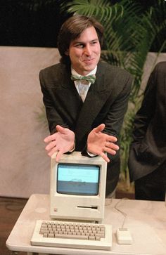 a man in a suit and bow tie holding his hands out to an old computer