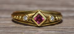 The Nashua: Etruscan Style Tourmaline Ring with Diamonds. The center is bezel set with a carre cut tourmaline with points at the directions of the compass. On either side of the center are bezel set round brilliant cut diamonds with three granulation's on either side. The ring is finished with a drop down to the edge and a sandblasted finish. Etruscan Jewelry, Cute Engagement Rings, The Compass, Tourmaline Ring, Gems Jewelry, Custom Engagement Ring, Round Brilliant Cut Diamond, Brilliant Cut Diamond, Cute Jewelry