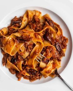 a white plate topped with pasta covered in meat and sauce next to a silver fork