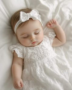 a baby wearing a white dress laying on top of a bed