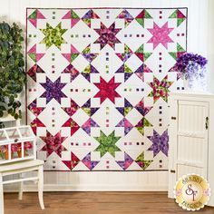 a quilted wall hanging next to a white cabinet and potted plant with purple flowers