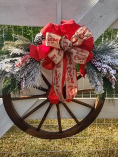 a wagon wheel decorated with red ribbon and pine cones is hanging on the side of a white fence