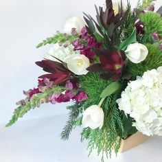 a bouquet of white and purple flowers in a wooden vase with greenery on the side