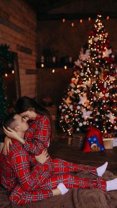 a man and woman in matching pajamas sitting next to a christmas tree