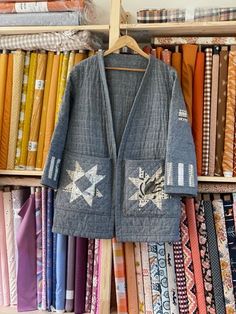 an open jacket hanging on a clothes rack in front of many different colored fabrics and ties