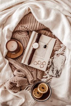 an open book, orange slices and other items on a bed with a white blanket