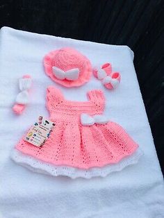 a pink crocheted baby dress and hat on a white blanket next to other items