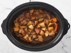 a crock pot filled with meat and potatoes on top of a marble countertop