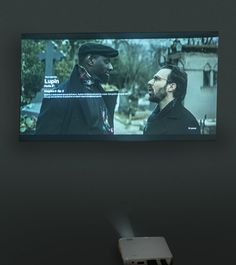 two men are talking in front of a large screen with the same image on it