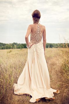 a woman in a long dress is walking through the grass with her back to the camera