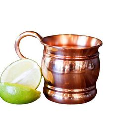 a metal cup with a lime next to it on a white background and an apple in the foreground