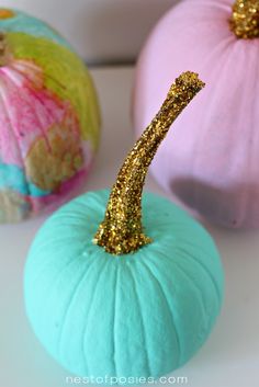 three painted pumpkins with gold glitter numbers on them, one blue and one pink