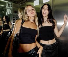 two beautiful women standing next to each other in front of a metal wall and elevator