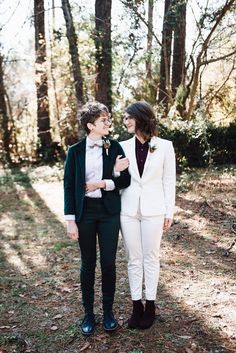 two women standing next to each other in the woods wearing white suits and black shoes