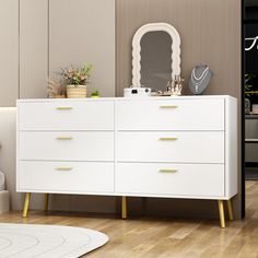 a white dresser sitting on top of a hard wood floor next to a mirror and potted plant