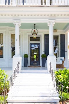 the front porch of a white house with blue shutters and potted plants on either side