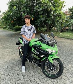 a young man sitting on top of a green and black sports bike in front of some trees