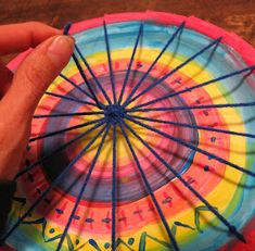 a hand holding a colorful paper plate with blue string on it and another hand touching the top