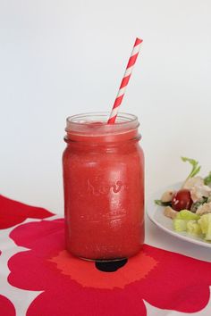 a red mason jar with a striped straw next to a salad on a tablecloth