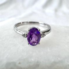 an oval shaped amethorate and diamond ring on a white surface with the center stone surrounded by three smaller round diamonds