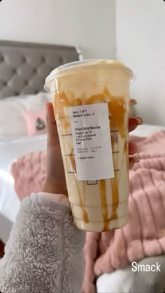 a person holding up a cup with caramel sauce on it in front of a bed