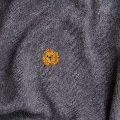 a small yellow flower sitting on the back of a gray sweater with an embroidered lion head