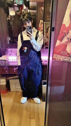 a man in overalls taking a selfie with his cell phone while standing in front of a mirror