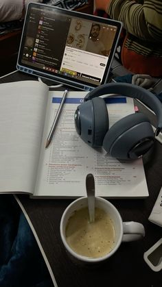 an open book with headphones on it next to a cup of coffee