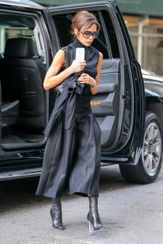 a woman standing in front of a car looking at her cell phone while wearing high heels