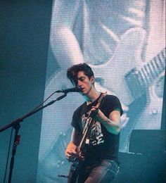 a man standing in front of a microphone on top of a stage next to a guitar