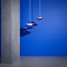 three hanging lights in the middle of a room with blue walls and concrete columns on either side