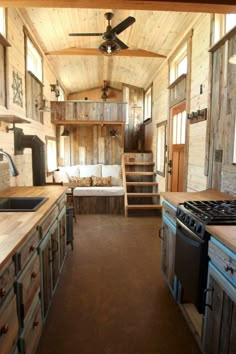 the interior of a tiny home with wood paneling and ceiling fan, stove top oven, sink, and refrigerator