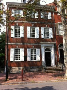 an old brick building with white shutters on the front and second story, next to a tree